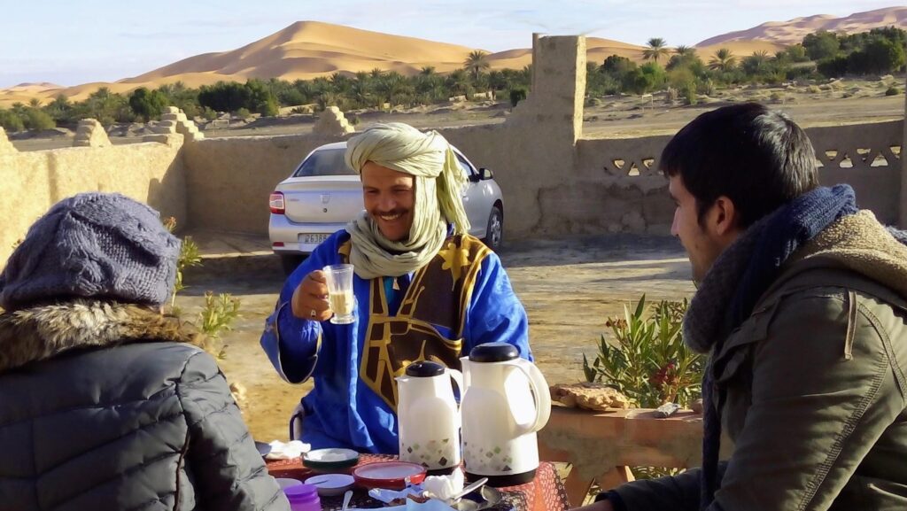 Ali partage le petit-déjeuner avec ses hôtes sur la terrasse de l'auberge La Vallée des Dunes, face aux dunes du Sahara